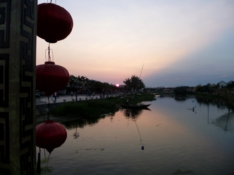 Sunset in Hoi An, Vietnam, a man on a fishing boat in the water in front of the sun