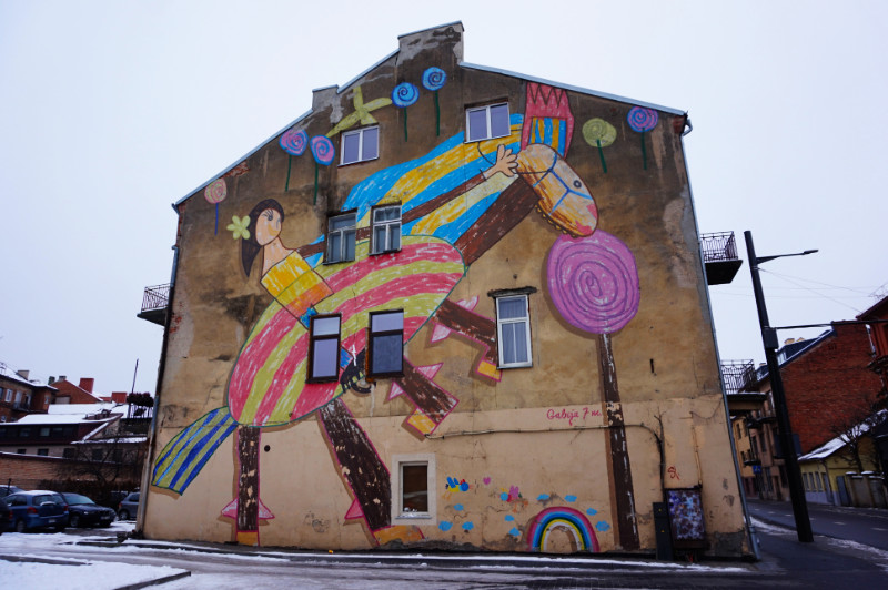 Street art in Kaunas, Lithuania. It's a child's drawing of a girl on a colourful rearing horse with a big purple lollipop.