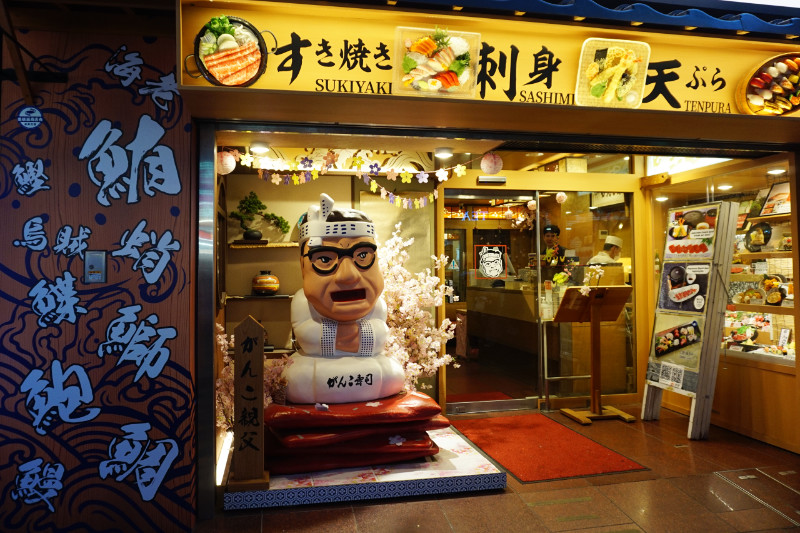 Restaurant in Dotonbori, Osaka, Japan. A statue of a Japanese man sits on a mat outside.