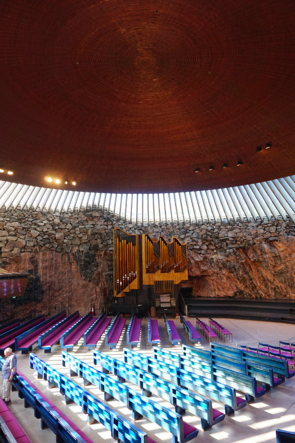 Temppeliaukio rock church, Helsinki, Finland. This is a portrait photo with the top half photo being the copper dome, the middle with the windows, rock and organ, and below being the colourful benches with scattered light on them from the windows.