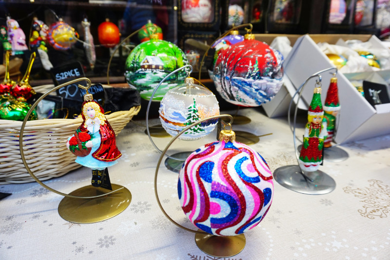 Glass baubles at the Christmas markets, Wroclaw, Poland. There are several baubles on display, one with swirly coloured patterns, one with frosted glass with a snowy tree scene painted on, a green one with a house and stream, a red one with snowy trees, and several people-shaped ones.