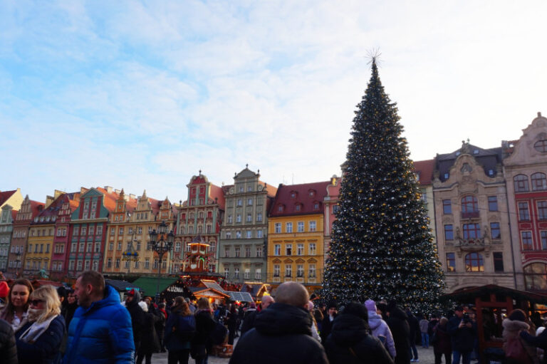 Rynek Square, Wroclaw Poland. There is a massive Christmas tree and a row of colourful buildings behind it.