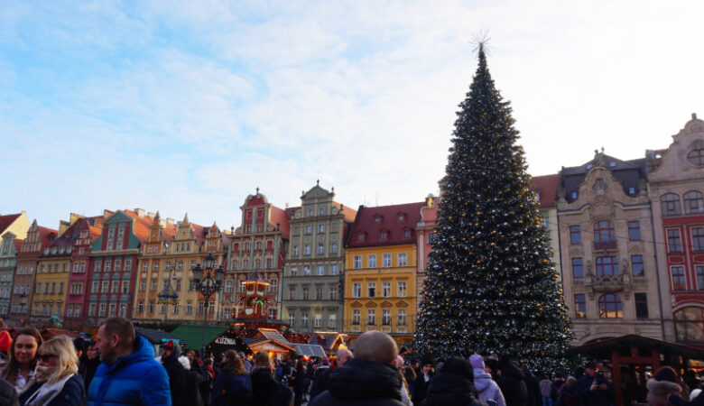 Rynek Square, Wroclaw Poland. There is a massive Christmas tree and a row of colourful buildings behind it.