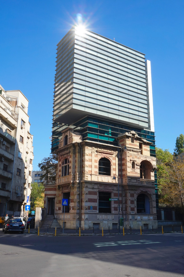 Interesting building by Revolution Square, Bucharest, Romania. The bottom half is a striped brick building with beige and orange stripes. Plonked on top is a grey glass building.