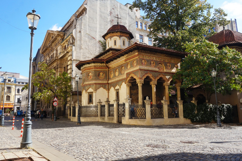 Stavropoleos Strada, Bucharest, Romania. It is a cobbled street with a monastery on the right with a couple of trees, and a lamppost on the left.