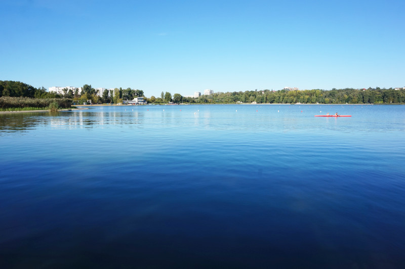 Lake in Valea Morilor Park, Chisinau, Moldova. The water is very blue and shimmering, and someone is kayaking.