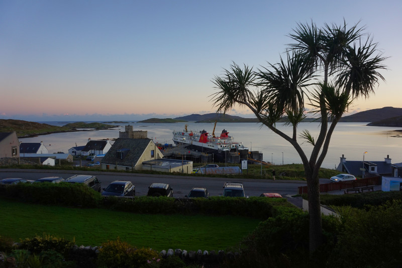 Castlebay, Barra, Scotland. Overlooking Kisimul Bay at sunset with the ferry docked at the port. On the right hand side is a kind of palm tree.